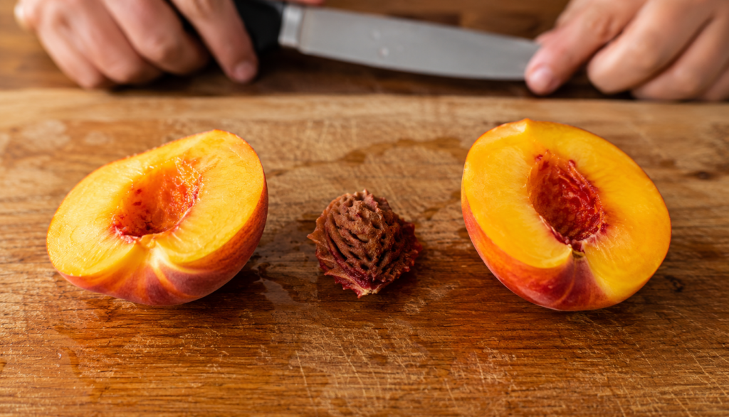  Peach pit removed on cutting board with flesh sliced on both sides