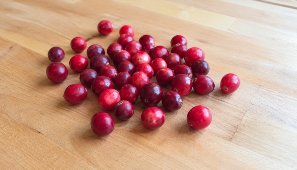 Fresh raw cranberries scattered on light wooden kitchen counter