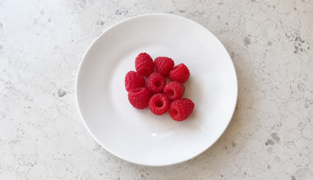 Small precise portion of fresh raspberries on white ceramic plate
