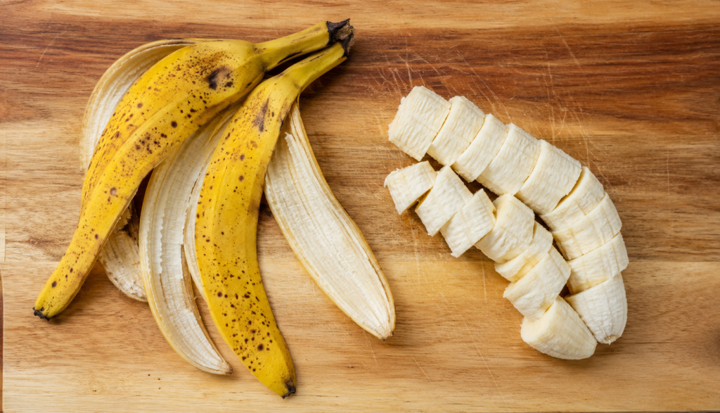 Banana peel separated from sliced flesh on wooden cutting board