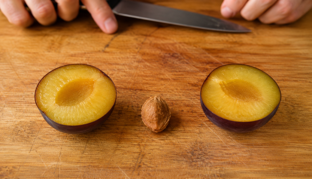 Small plum pit removed on cutting board with flesh sliced on both sides