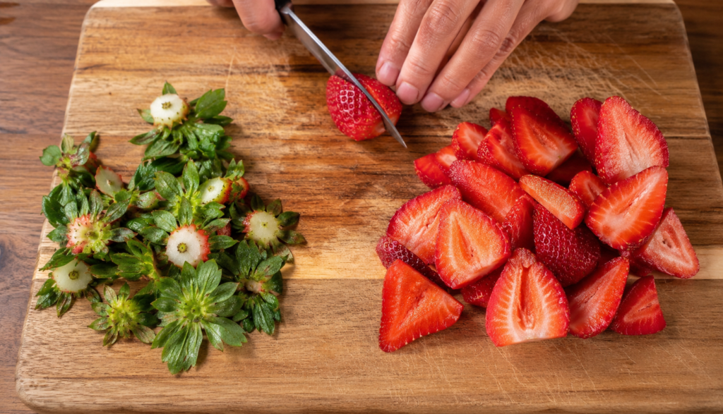 Strawberries sliced with green tops separated on wooden cutting board
