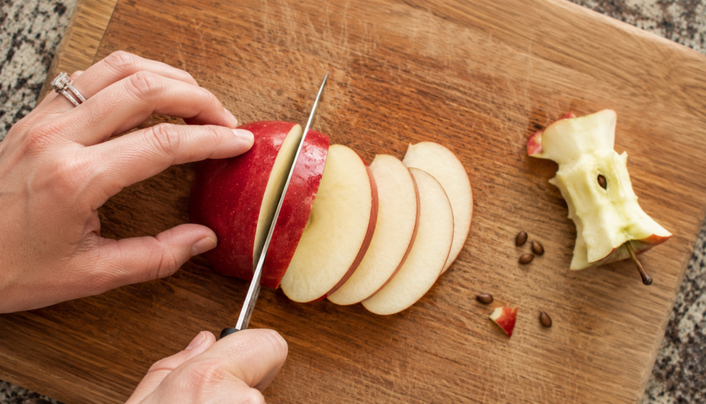 Hands slicing red apple on cutting board with core and seeds removed